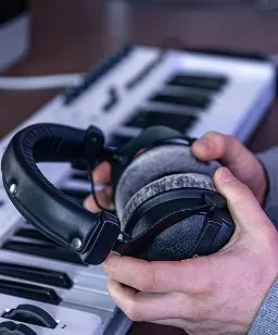 Mani che tengono cuffie sopra una tastiera MIDI