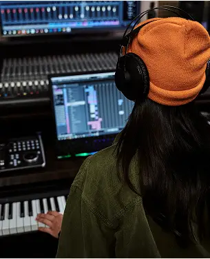 Producer con cuffie e tastiera MIDI davanti a workstation